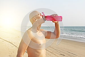 A bald, handsome man with a bare or bare torso is drinking water