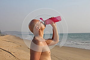 A bald, handsome man with a bare or bare torso is drinking water