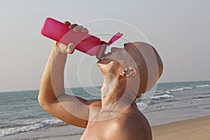 A bald, handsome man with a bare or bare torso is drinking water