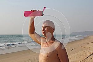 A bald, handsome man with a naked or bare torso watering himself