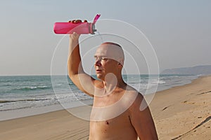 A bald, handsome man with a naked or bare torso watering himself