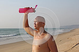A bald, handsome man with a naked or bare torso watering himself