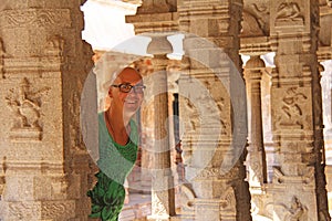 A bald and handsome tourist man wearing glasses, inside the Temple of Virupaksha, among the carved columns of the Temple