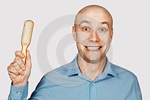 Bald man with alopecia holds a comb in his hand. concept absurdity