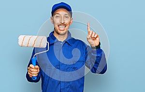 Bald man with beard holding roller painter surprised with an idea or question pointing finger with happy face, number one