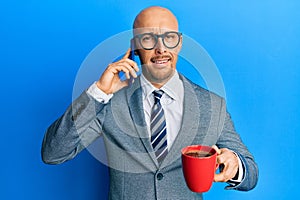 Bald man with beard using smartphone and drinking a cup of coffee clueless and confused expression