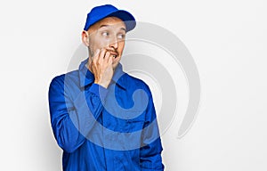 Bald man with beard wearing builder jumpsuit uniform looking stressed and nervous with hands on mouth biting nails