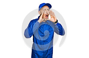 Bald man with beard wearing builder jumpsuit uniform shouting angry out loud with hands over mouth