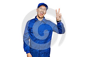 Bald man with beard wearing builder jumpsuit uniform smiling with happy face winking at the camera doing victory sign with fingers