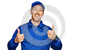 Bald man with beard wearing builder jumpsuit uniform success sign doing positive gesture with hand, thumbs up smiling and happy