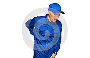 Bald man with beard wearing builder jumpsuit uniform suffering of backache, touching back with hand, muscular pain