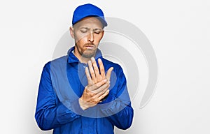 Bald man with beard wearing builder jumpsuit uniform suffering pain on hands and fingers, arthritis inflammation