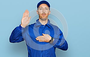 Bald man with beard wearing builder jumpsuit uniform swearing with hand on chest and open palm, making a loyalty promise oath