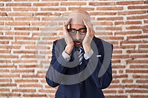 Bald man with beard wearing business clothes and glasses with sad expression covering face with hands while crying