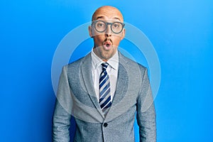 Bald man with beard wearing business jacket and glasses scared and amazed with open mouth for surprise, disbelief face