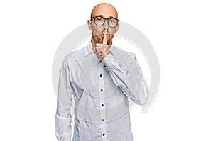 Bald man with beard wearing business shirt and glasses asking to be quiet with finger on lips