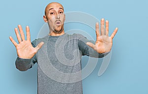 Bald man with beard wearing casual clothes afraid and terrified with fear expression stop gesture with hands, shouting in shock