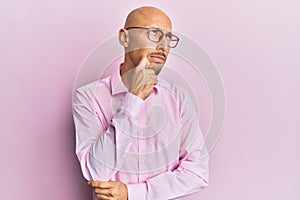 Bald man with beard wearing casual clothes and glasses thinking concentrated about doubt with finger on chin and looking up