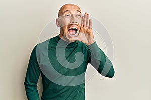 Bald man with beard wearing casual turtleneck sweater shouting and screaming loud to side with hand on mouth