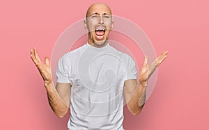 Bald man with beard wearing casual white t shirt crazy and mad shouting and yelling with aggressive expression and arms raised