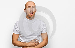 Bald man with beard wearing casual white t shirt with hand on stomach because nausea, painful disease feeling unwell