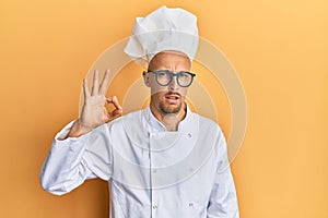 Bald man with beard wearing professional cook apron doing ok gesture clueless and confused expression