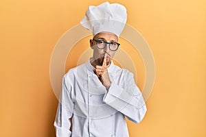 Bald man with beard wearing professional cook uniform asking to be quiet with finger on lips