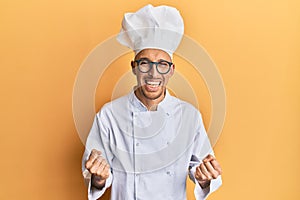 Bald man with beard wearing professional cook uniform very happy and excited doing winner gesture with arms raised, smiling and