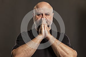 The bald man folded his hands in prayer by his face. Faith and hope. Dark background