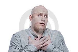 A bald man in a gray shirt pressed his hands to his chest in surprise. Isolated on a white background. Close-up