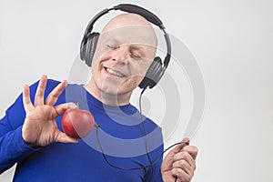 Bald man with headphones listens to music through a red apple player. Metaphor and concept of vitamin benefits in music and sound