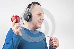 Bald man with headphones listens to music through a red apple player. Metaphor and concept of vitamin benefits in music and sound