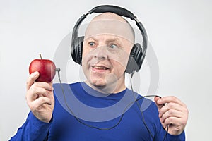 Bald man with headphones listens to music through a red apple player. Metaphor and concept of vitamin benefits in music and sound