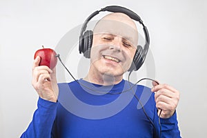 Bald man with headphones listens to music through a red apple player. Metaphor and concept of vitamin benefits in music and sound