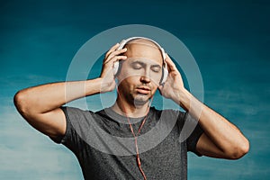A bald man listens and enjoys music in large headphones with his eyes closed on a greenish background