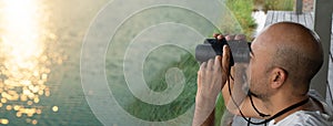 Bald man looking trough binocular for explore in lake nature relaxation in summer season banner background