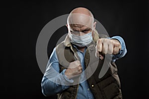 Bald man in a medical mask in a fighting stance. A blow to the disease. Self-isolation during the coronavirus pandemic. Black