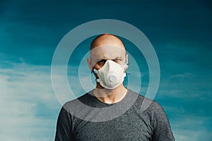 A bald man in a respirator on a blue background menacingly looks sneakily