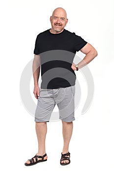 Bald man with sandals t-shirt and shorts, hand on hip looking at camera on whithe background