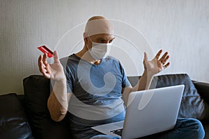 Bald man sitting in medical mask laptop with credit card in hand