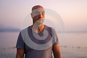 Bald man standing on beach and looking at amazing sunset and sea with calm