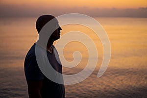 Bald man standing on beach and looking at amazing sunset and sea with calm