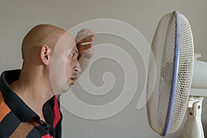 Bald man sweating because summer heat haze. Man refreshing in front of air electric fan