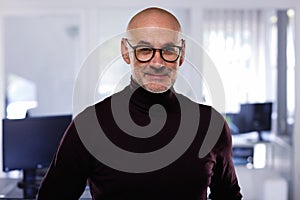 Bald man wearing turtleneck sweater and standing at the office