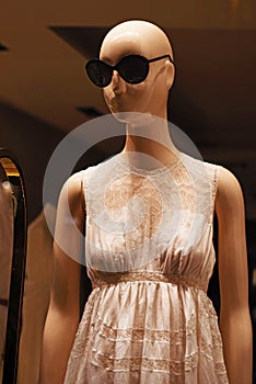 Bald mannequin in big sunglasses in a stylish dress in a shop window in Milan