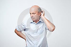 Bald mature man with mustache in blue shirt is suffering from indecision.