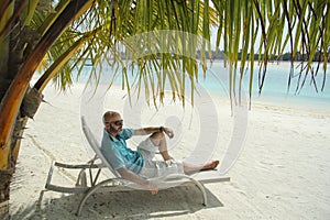Bald men on a sun lounger under a palm tree in the Maldivian b