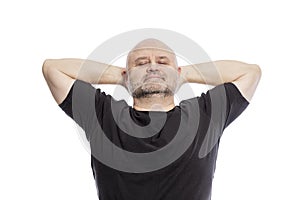 Bald middle-aged man in a black T-shirt, hands behind his head, smiling. Isolated over white background