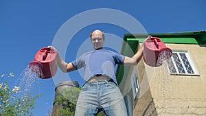 Bald mustachioed man joyfully watering the garden with red watering can