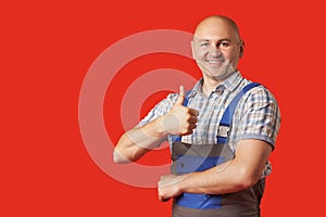 Bald, unshaven man in work clothes shows an ok hand gesture on a red background